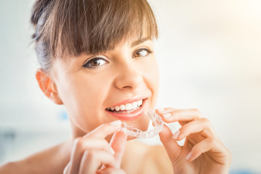 Smiling woman holding clear Invisalign aligner in a dental setting, highlighting orthodontic treatment options at Moon Orthodontics in Overland Park.